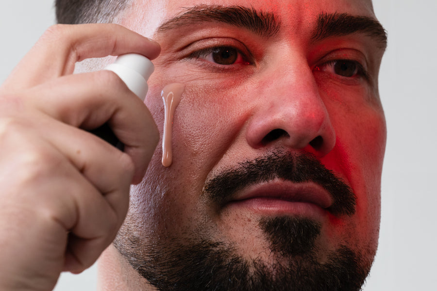 Man applying serum to his face under red LED light